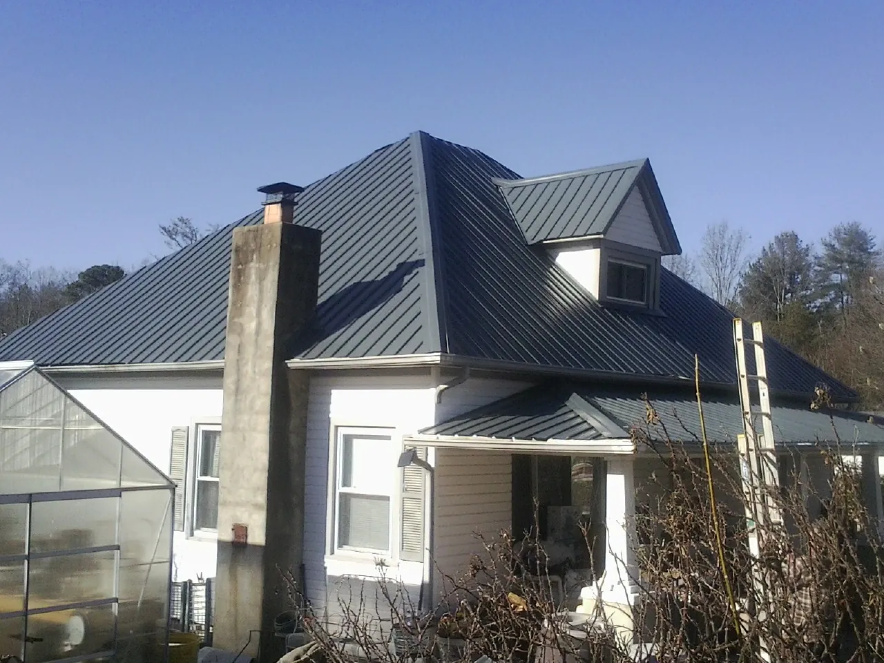 Dark blue standing seam metal roof on a white farmhouse with dormer — Slate & Tile Roof Repair by Roofing Brothers in Girard